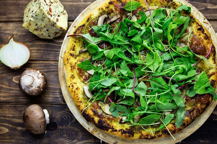 Domowa pizza z pesto z serem z suszonymi pomidorami, oregano i pieprzem oraz brązowymi pieczarkami, cebulą i świeżą rukolą